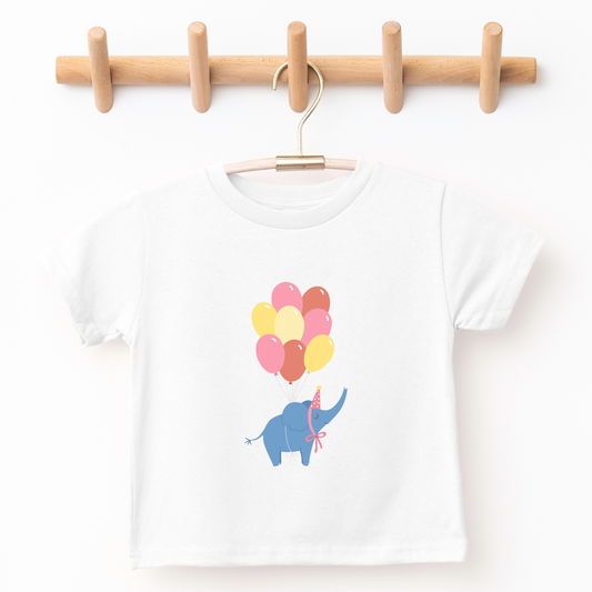 kid's graphic tee illustrated with balloon bunch holding up elephant wearing party hat in the air